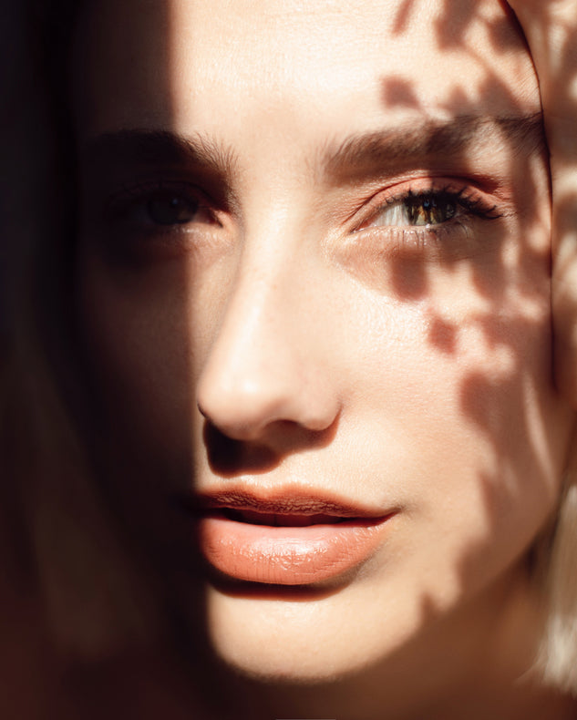 A woman's face covered partially by the shadows of leaves