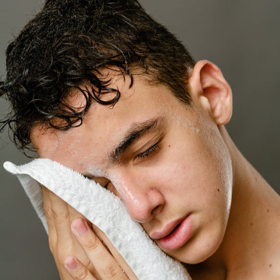A man holding a towel to his face after cleaning it with gentle face cleanser: Agave Ferment + Fruit Extract Face Cleanser.