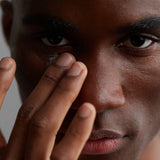 A dark-skinned man applying our lightweight moisturizer, Agave Stem Cell Lightweight Moisturizer, on his face.
