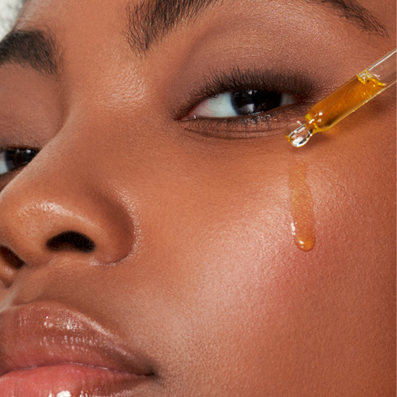 A dark skinned woman applying our face oil serum Cannacomplex™ Nourishing Face Serum on her face.